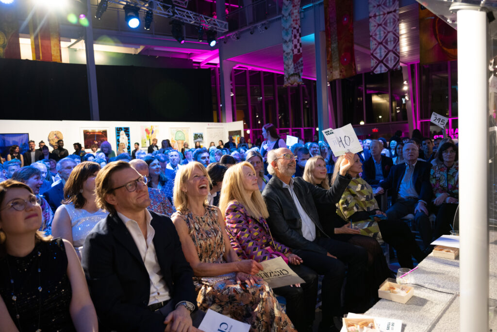 MassArt Auction guests smiling as they raise their bid numbers to donate to MassArt's scholarship fund.