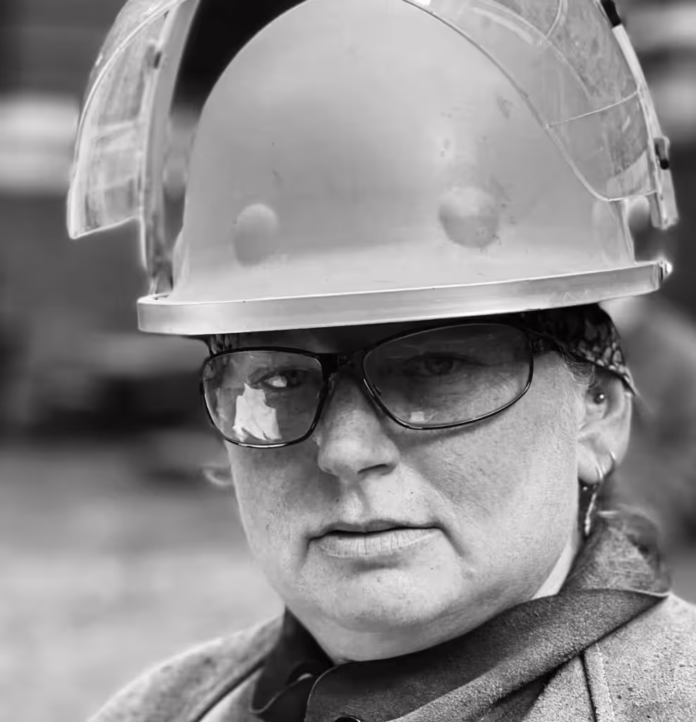 Black-and-white close-up of a person in a hard hat and safety glasses, embodying sustainability in the workplace.