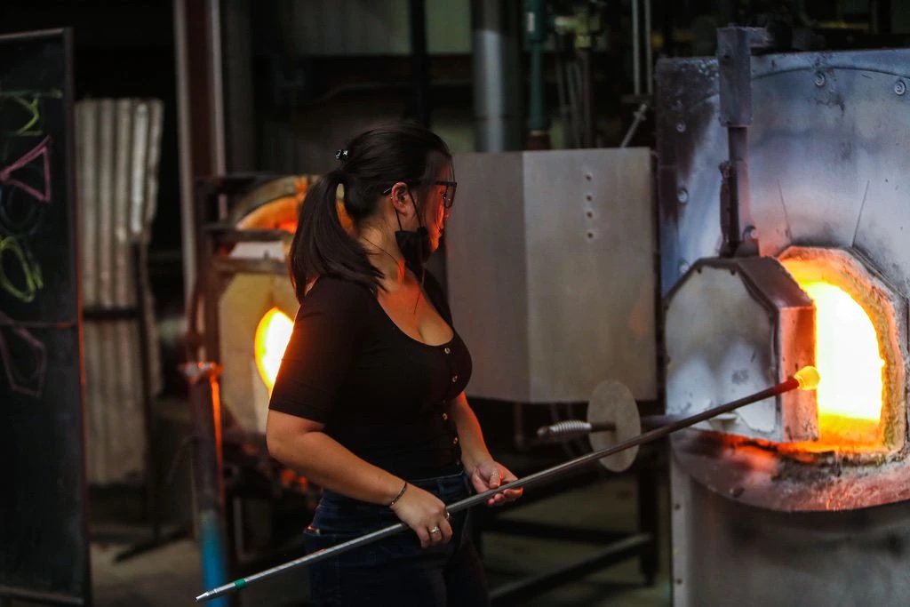 MassArt student Celia Delani is shown heating glass in the hot shop